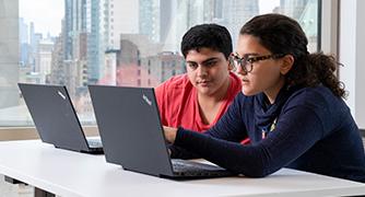 An image of two students on their laptops. 